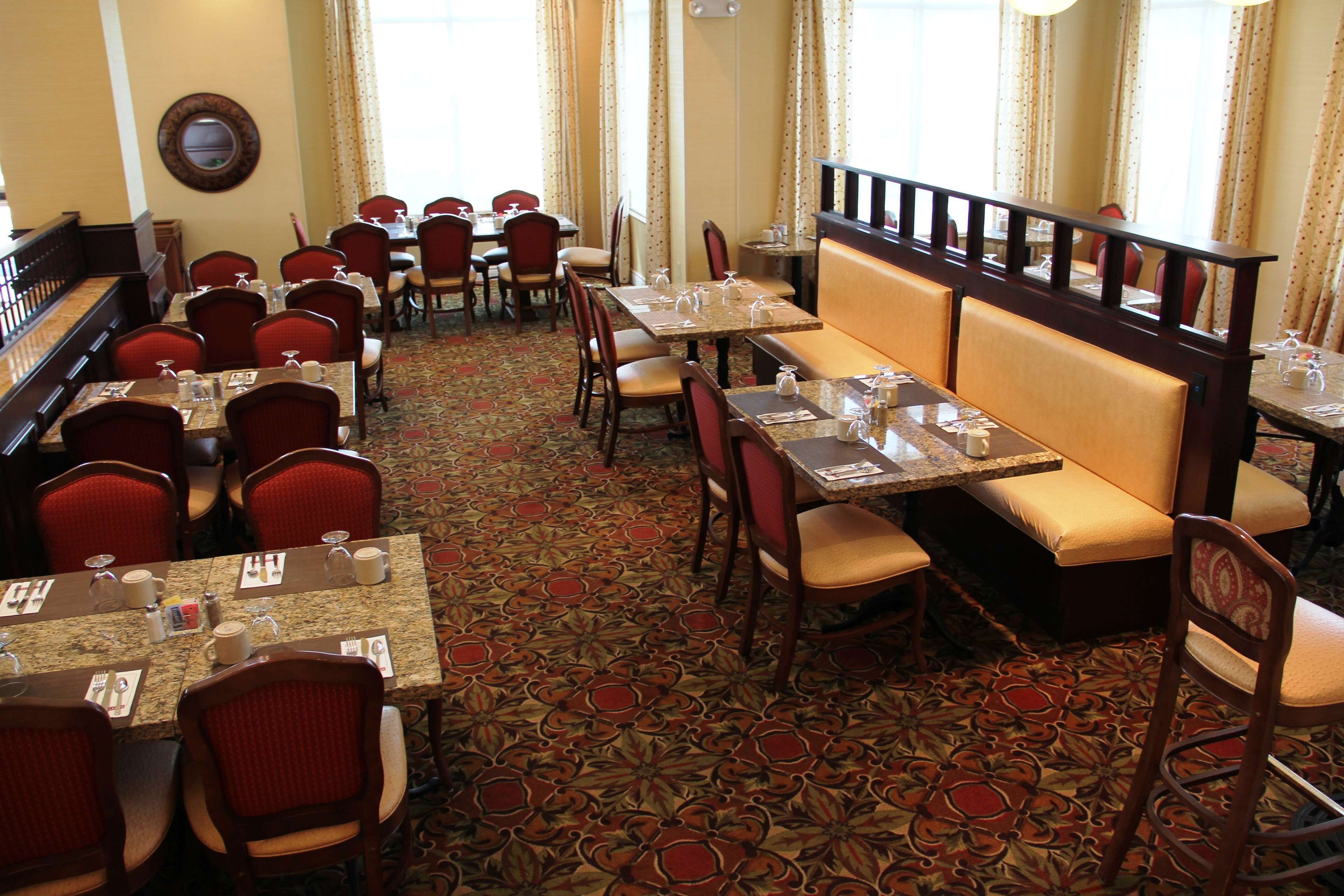 En restaurant med flere borde og båse, gulvbelagt med tæpper, og forskellige stole.