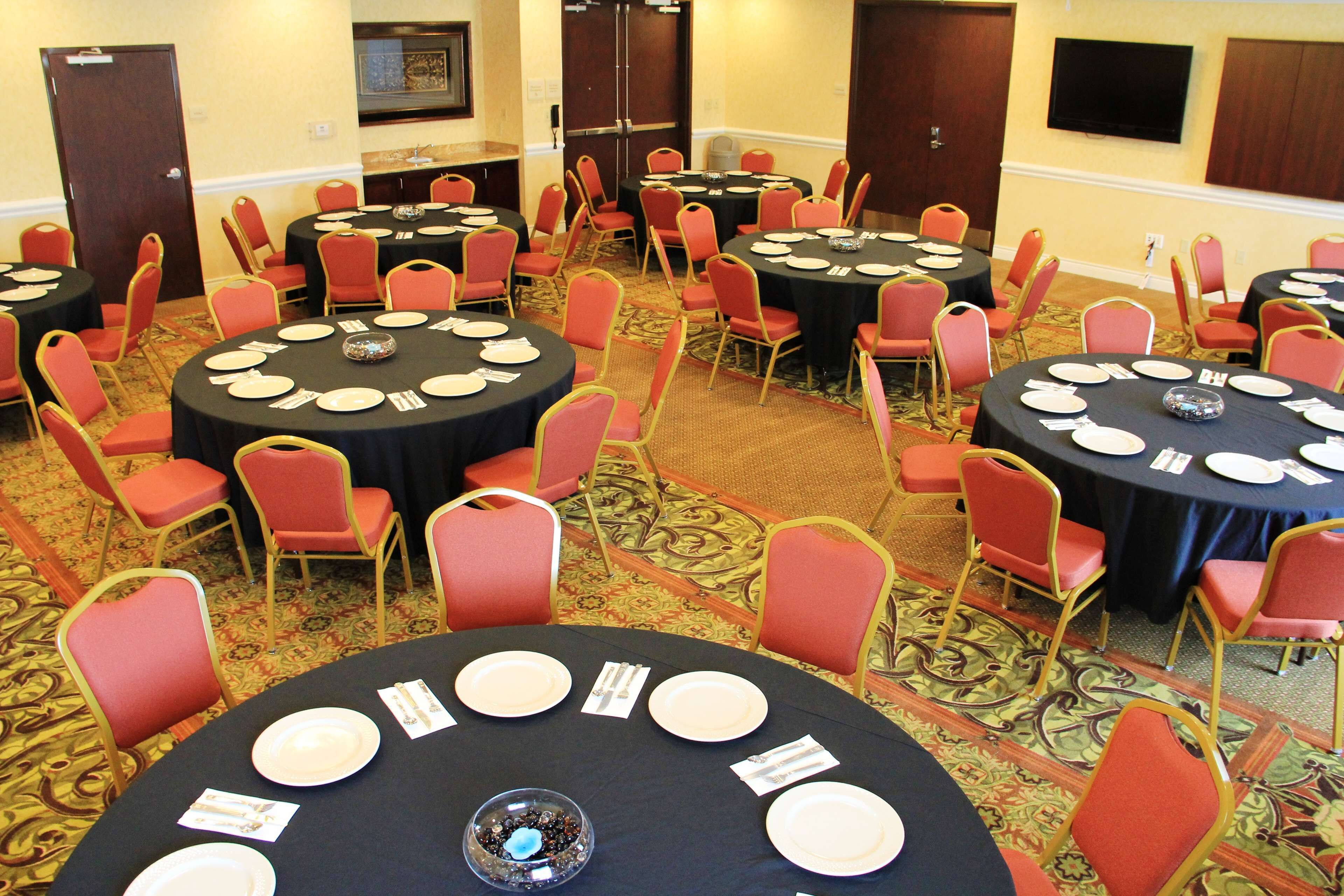 A conference room with multiple round tables, each set with plates, cutlery, and a centerpiece. Red chairs are arranged around the tables.