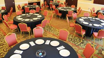A conference room with multiple round tables, each set with plates, cutlery, and a centerpiece. Red chairs are arranged around the tables.