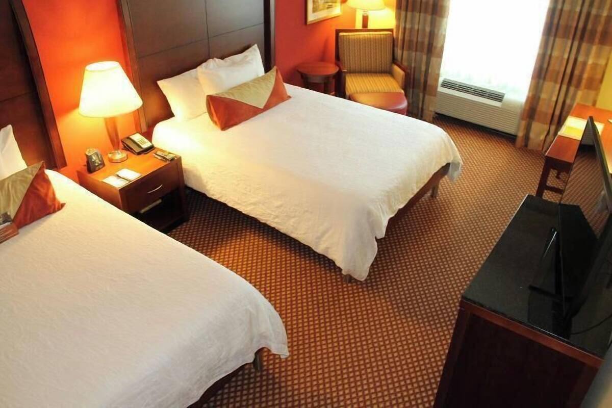 A hotel room with two beds, a desk, a chair, a lamp, and a television.