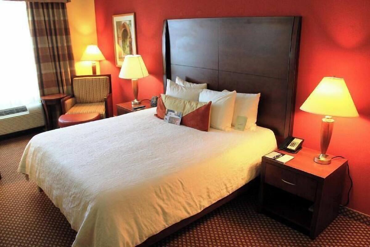 A hotel room with a large bed, two bedside tables with lamps, a chair, and a window with curtains.