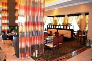 A hotel lobby with a dining area, a reception desk, and a decorative plant arrangement. - Hilton Garden Inn Houston West Katy (Katy)