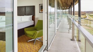 Habitación de hotel con cama, una silla verde y balcón con vistas al campo.