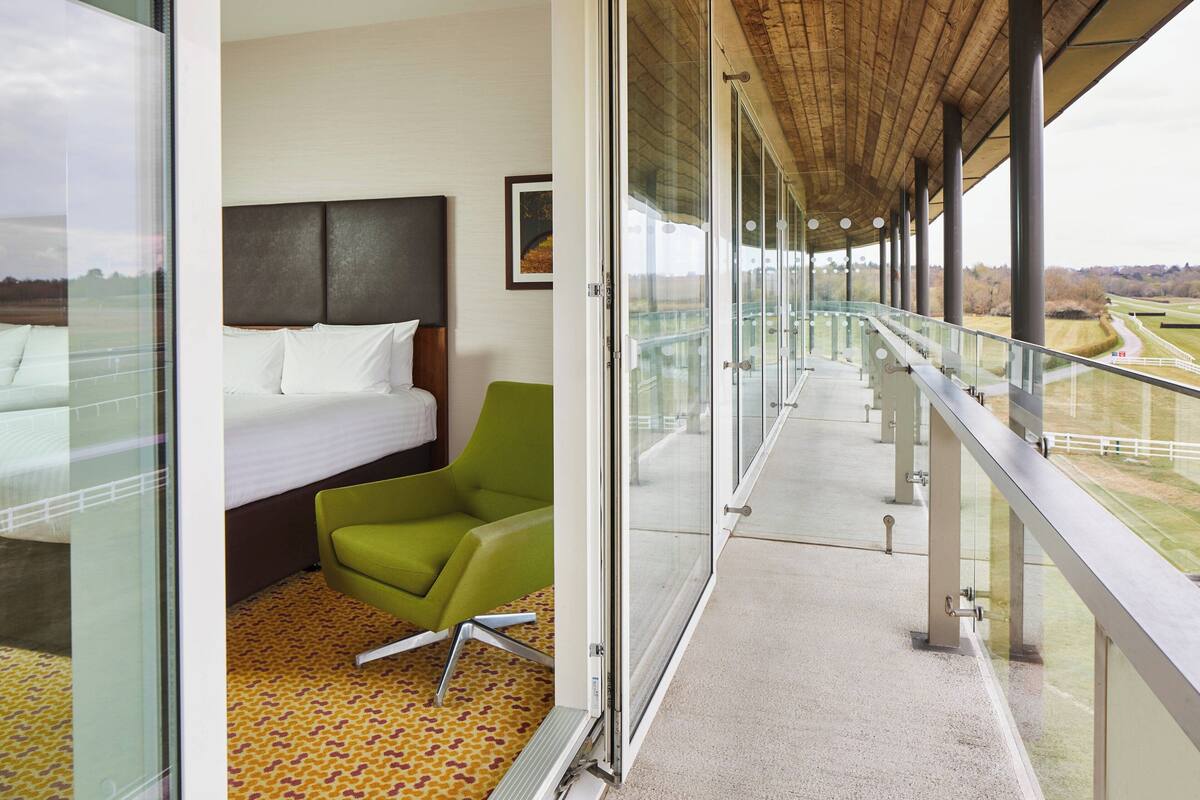 A hotel room with a bed, a green chair, and a balcony with a view of the countryside.