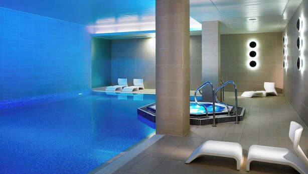 Una piscina interior moderna con un jacuzzi, sillas de descanso y suelo de baldosas.