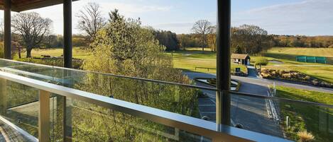 A view from a balcony with a glass railing overlooking a golf course.