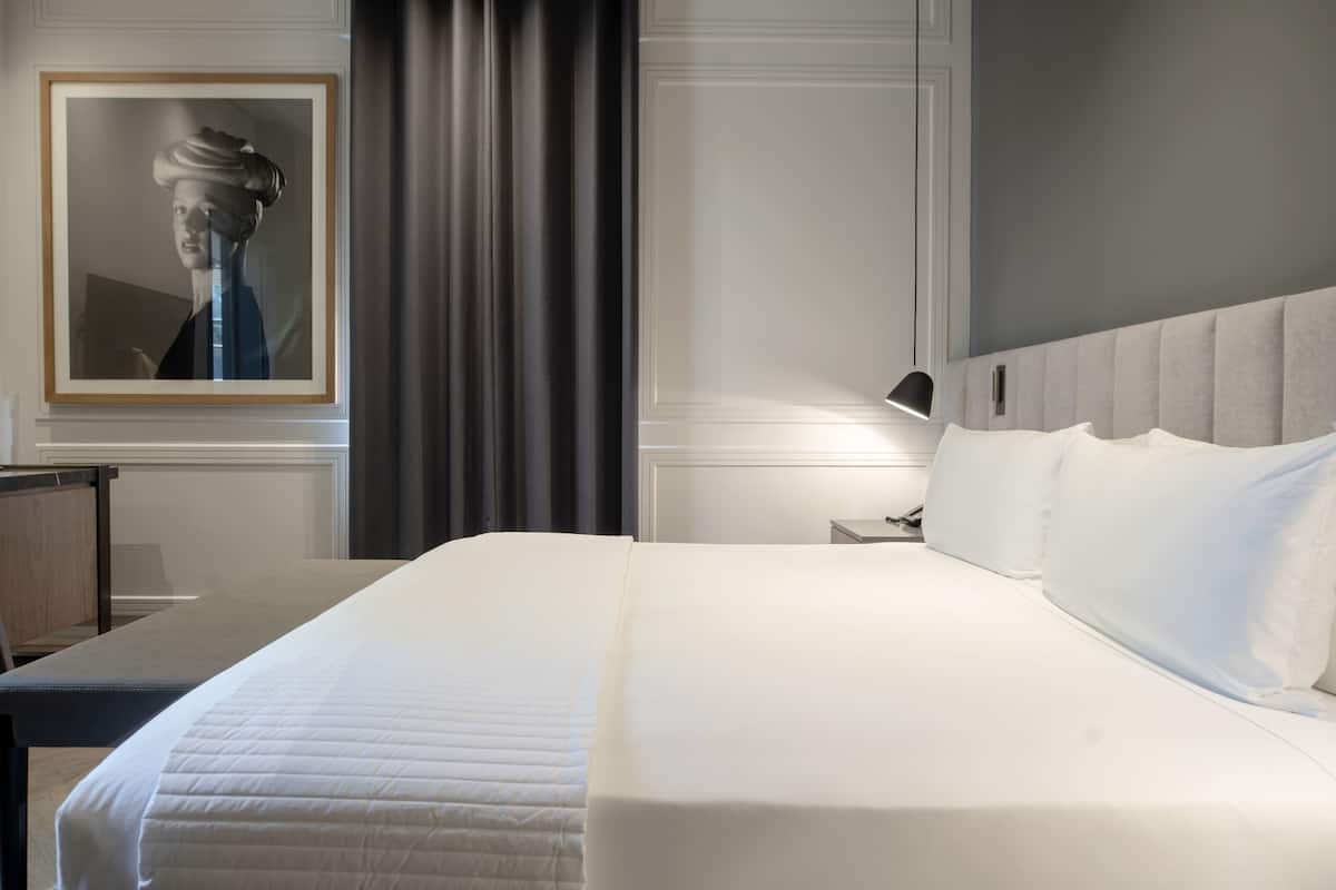 A neatly made bed with white linens, a headboard, and a bedside table with a lamp.