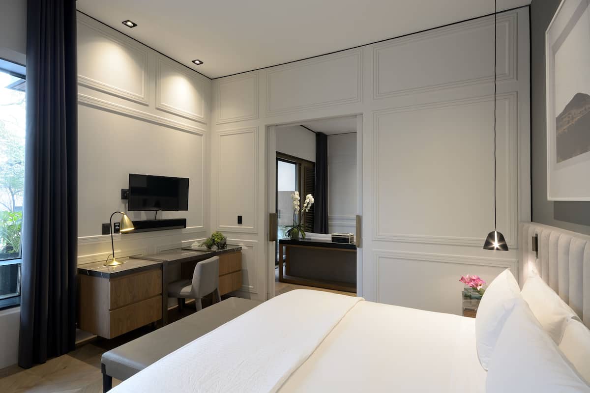 A modern hotel room with a large bed, a desk with a computer, a TV, and a bathroom visible through an open door.