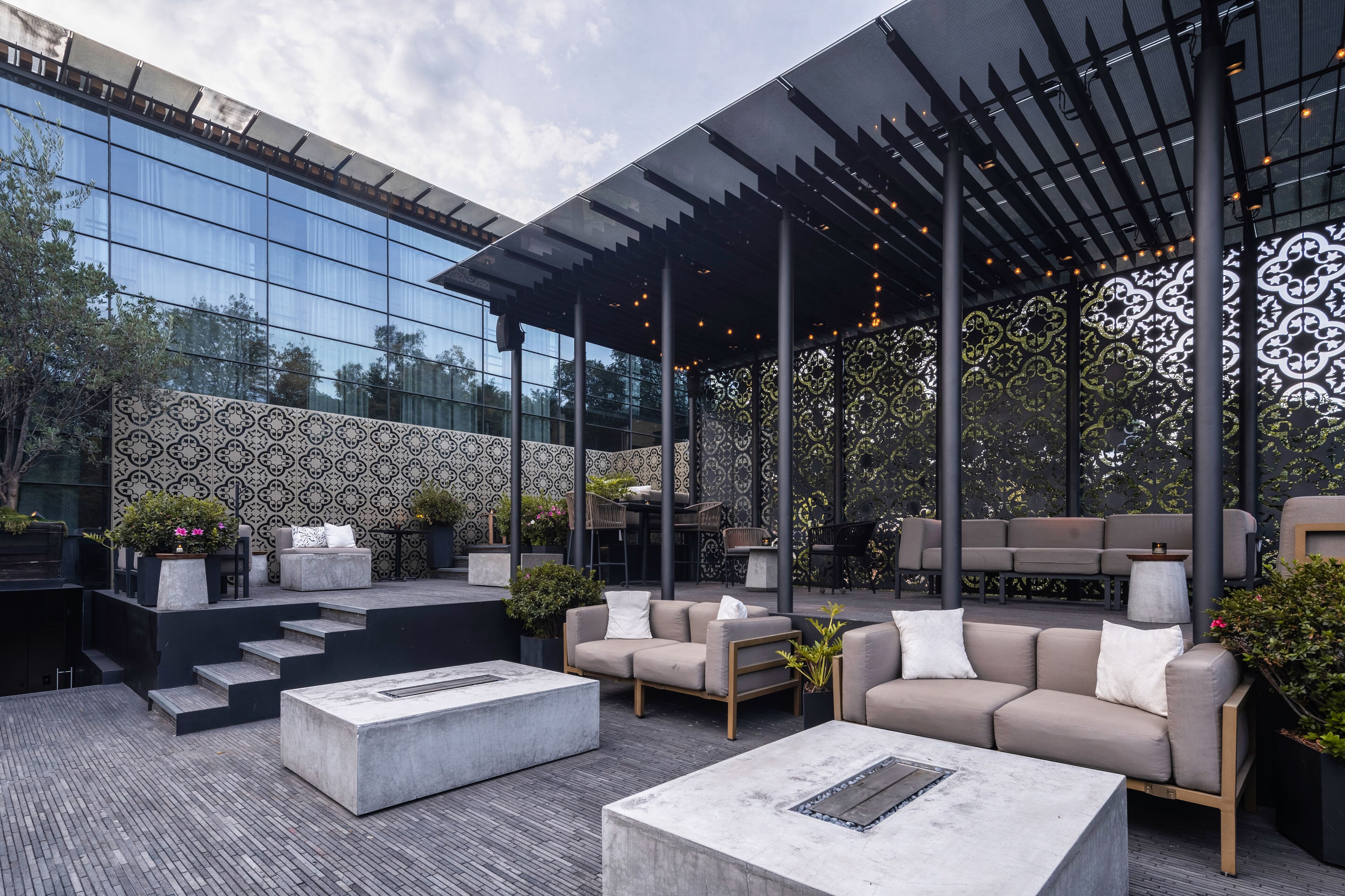 An outdoor seating area with modern furniture, a pergola, and a patterned wall.