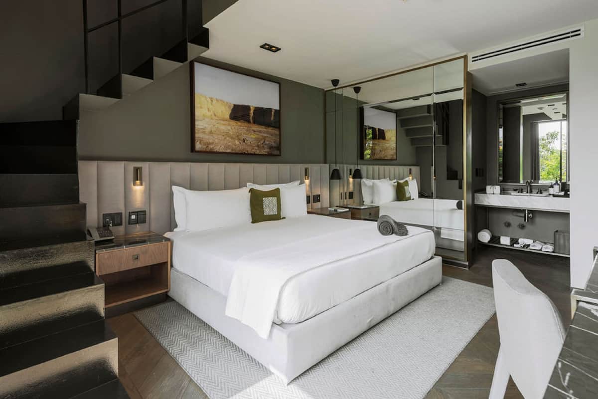 A modern bedroom with a large bed, a built-in desk, a mirror, and a staircase.