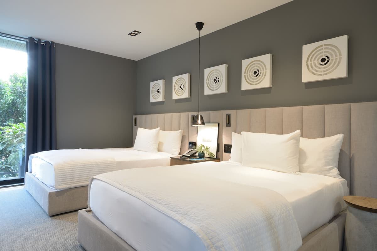A hotel room with two beds, a large window with curtains, and wall art.