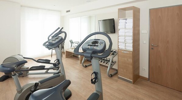 A room with two exercise bikes, a television, a wooden wardrobe, and a small table with a chair. - FourSide Hotel & Suites Vienna (Vienna)