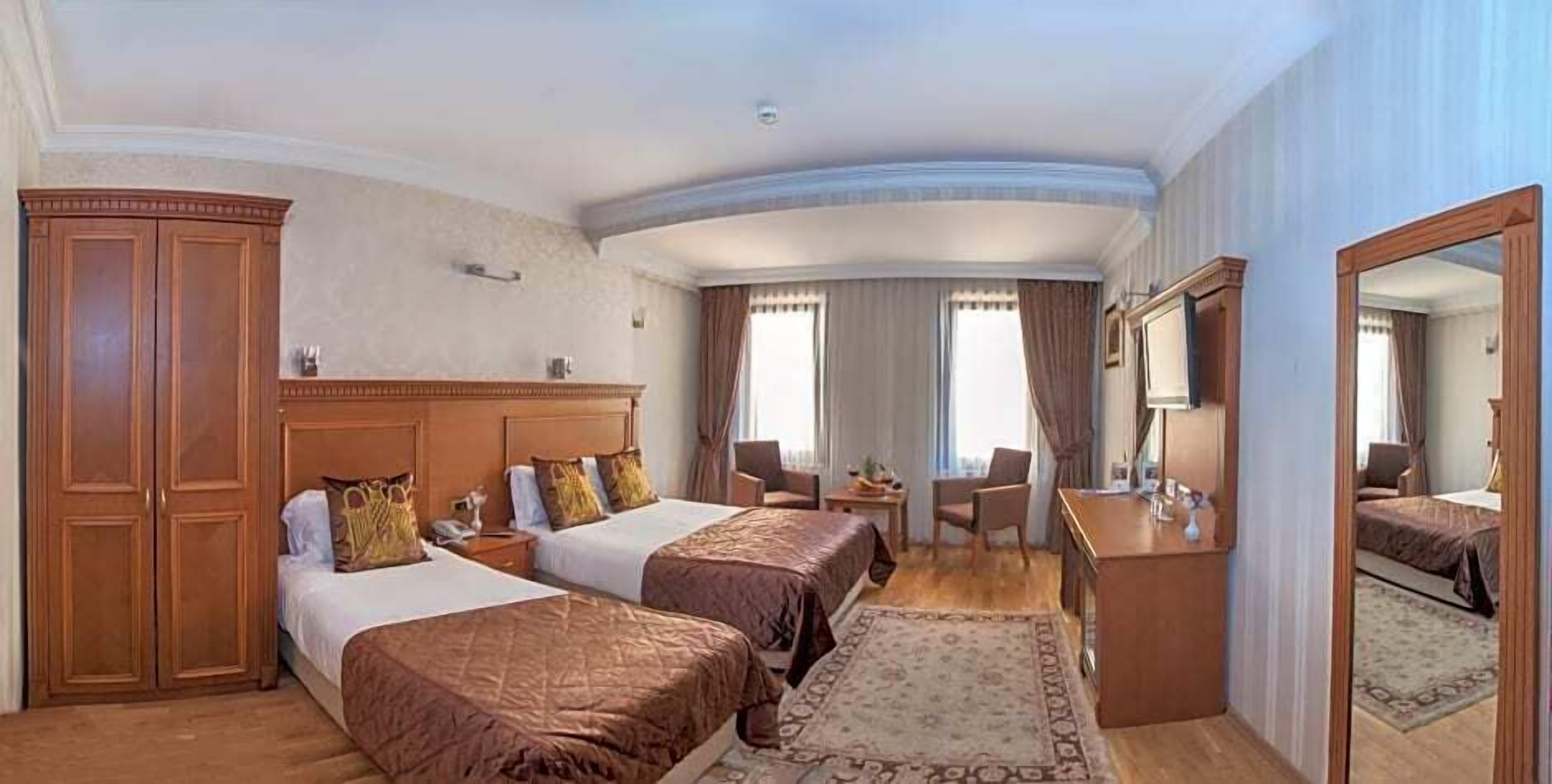 A hotel room with two beds, a desk, a chair, a wardrobe, and a large mirror.