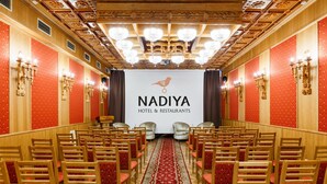 A conference room with rows of wooden chairs and red patterned carpets, a chandelier, and a banner reading "NADIYA HOTEL & RESTAURANTS". - Nadiya Hotel (Ivano-Frankivsk)