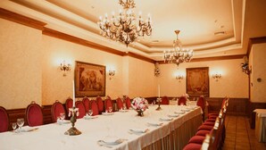 A long dining table set for a formal event, with red upholstered chairs and a chandelier overhead. - Nadiya Hotel (Ivano-Frankivsk)