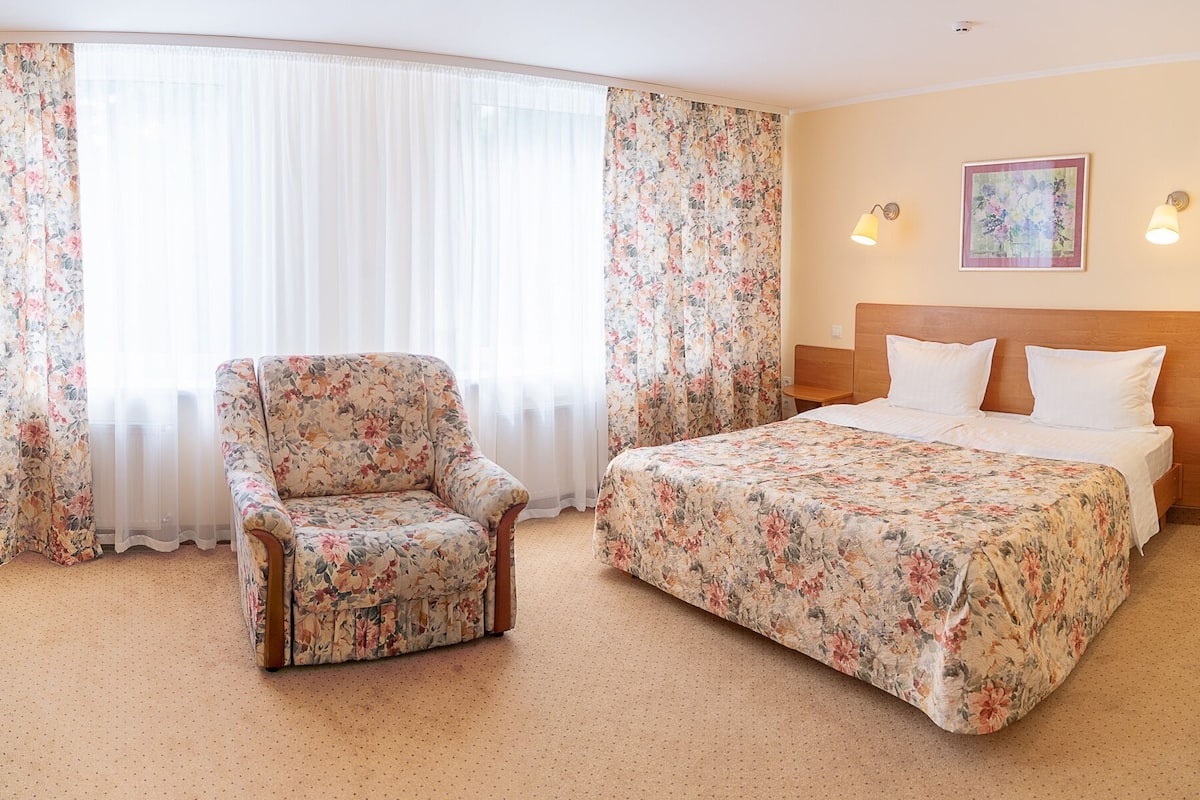 Quarto de hotel com cama, uma cadeira e cortinas.