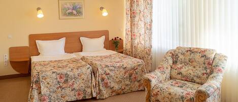 A hotel room with a bed, two bedside tables, a chair, a floral curtain, and a wall-mounted air conditioner.
