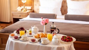 A neatly arranged breakfast table with croissants, fruits, and beverages in a hotel room with a tufted headboard and a bedside lamp. - Nadiya Hotel (Ivano-Frankivsk)