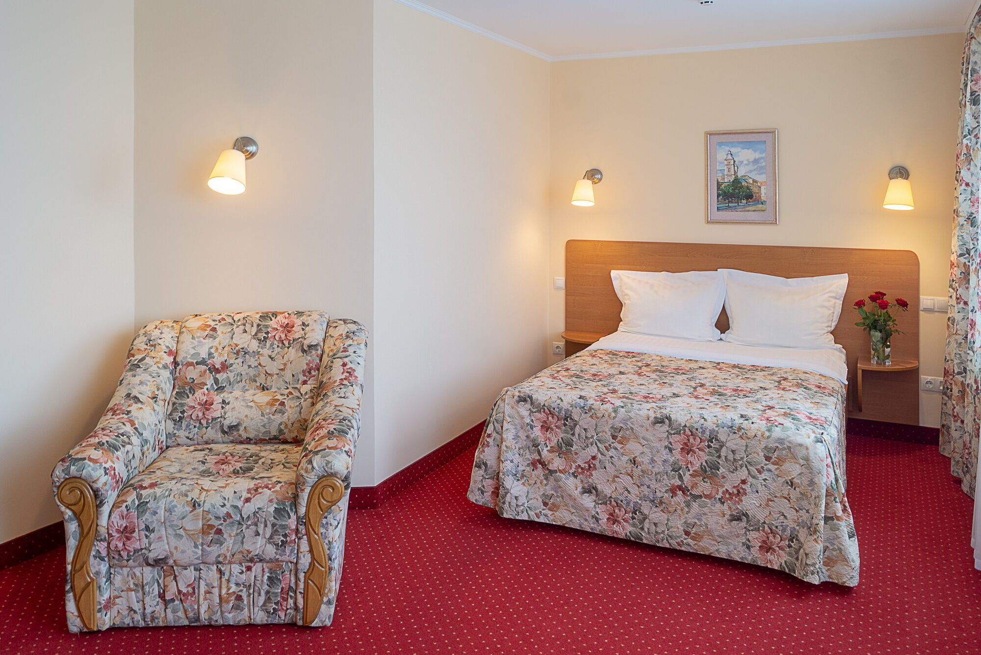 Una habitación de hotel con una cama, una silla y dos lámparas fijadas a la pared.