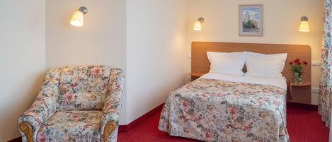 Una habitación de hotel con una cama, una silla y dos lámparas fijadas a la pared.