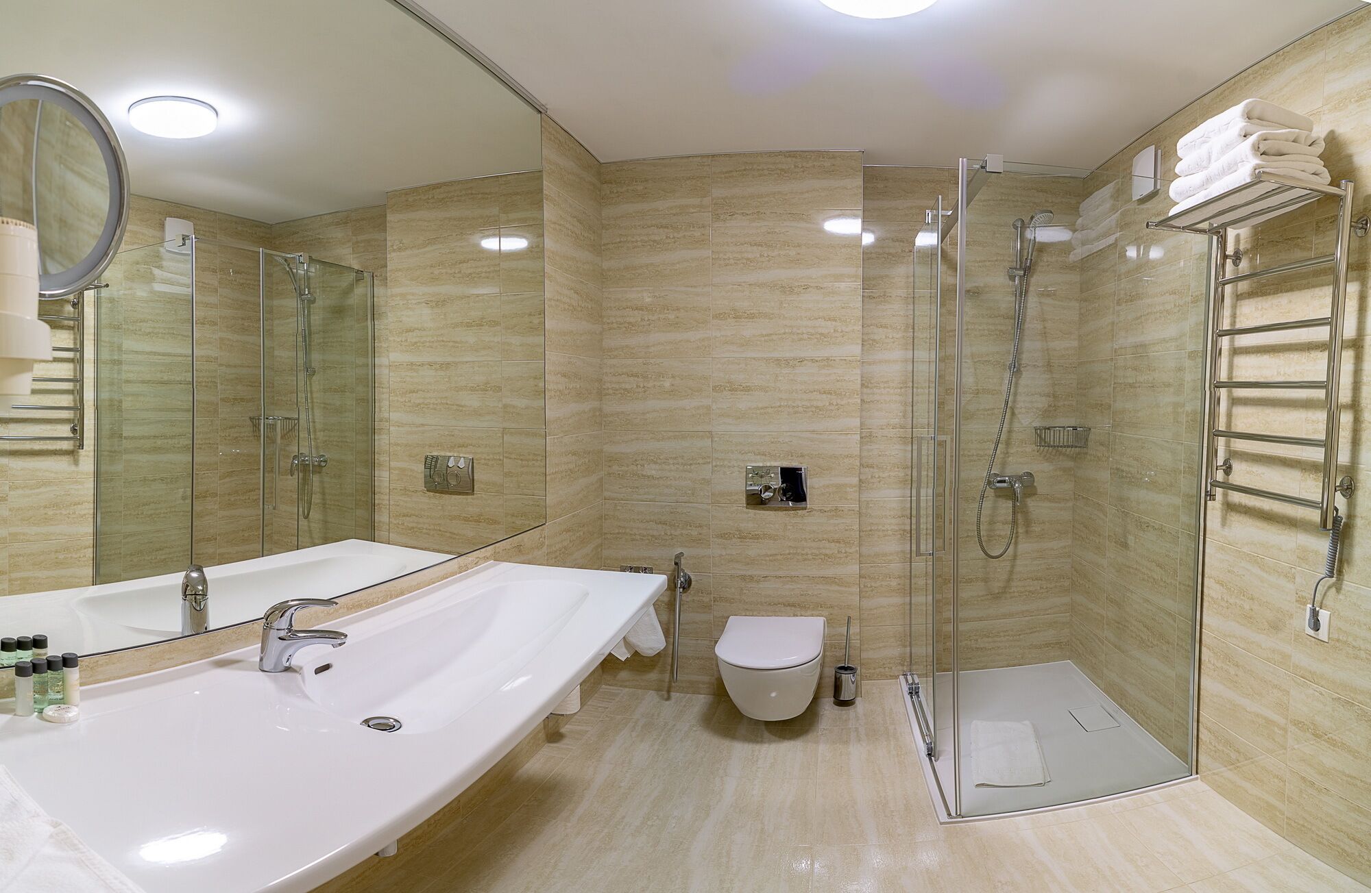 Une salle de bain moderne dotée d’un grand lavabo, de toilettes et d’une douche séparée par des parois en verre.