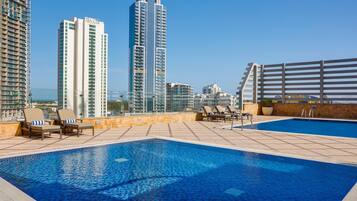 A rooftop swimming pool with lounge chairs and a view of high-rise buildings.