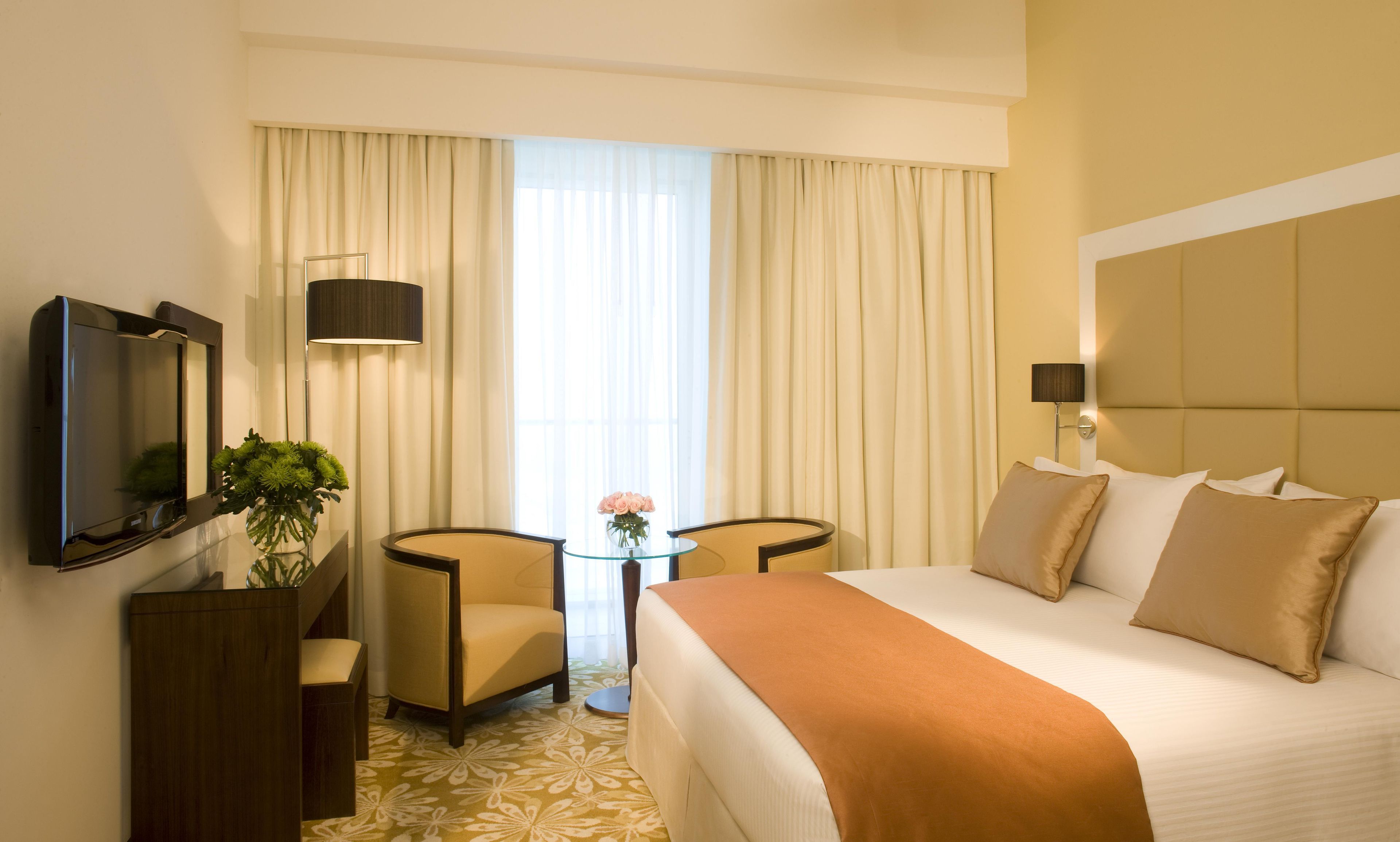 A hotel room with a bed, a desk, a chair, a TV, and a window with curtains.
