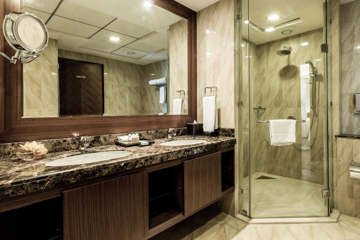 A modern bathroom with two sinks, a glass shower enclosure, and a toilet.