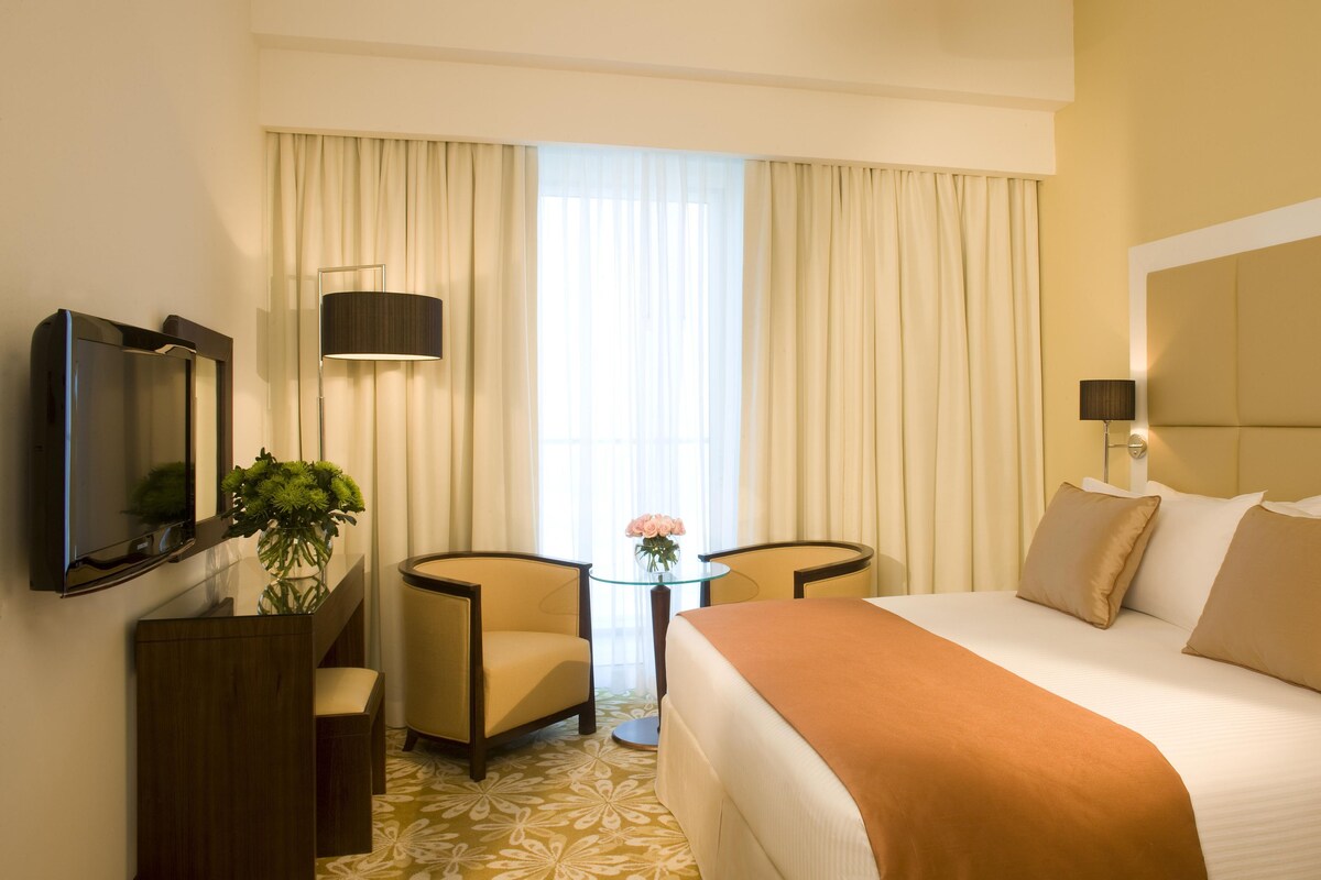 A hotel room with a bed, a desk, a chair, a TV, and a window with curtains.