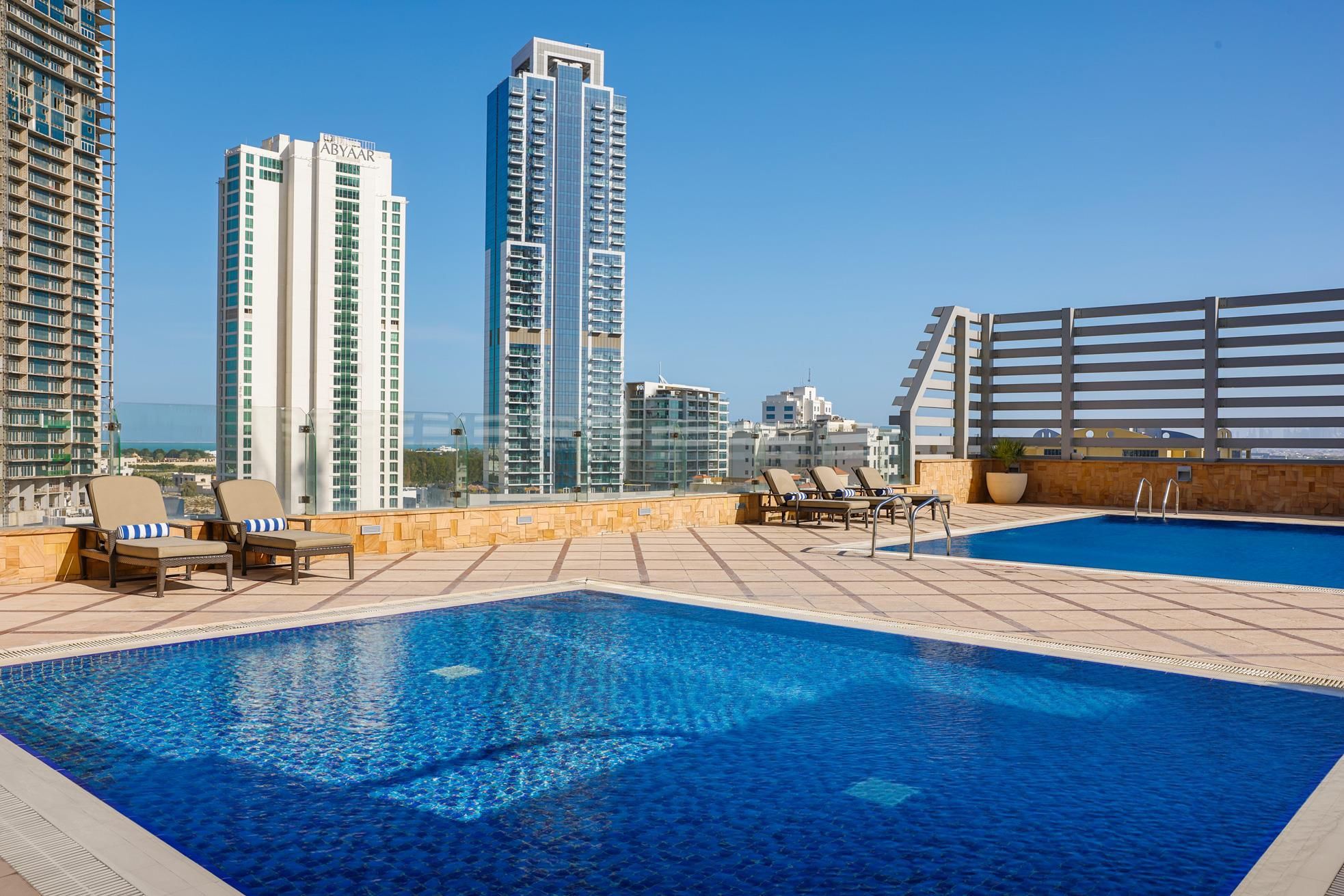 A rooftop swimming pool with lounge chairs and a view of high-rise buildings.
