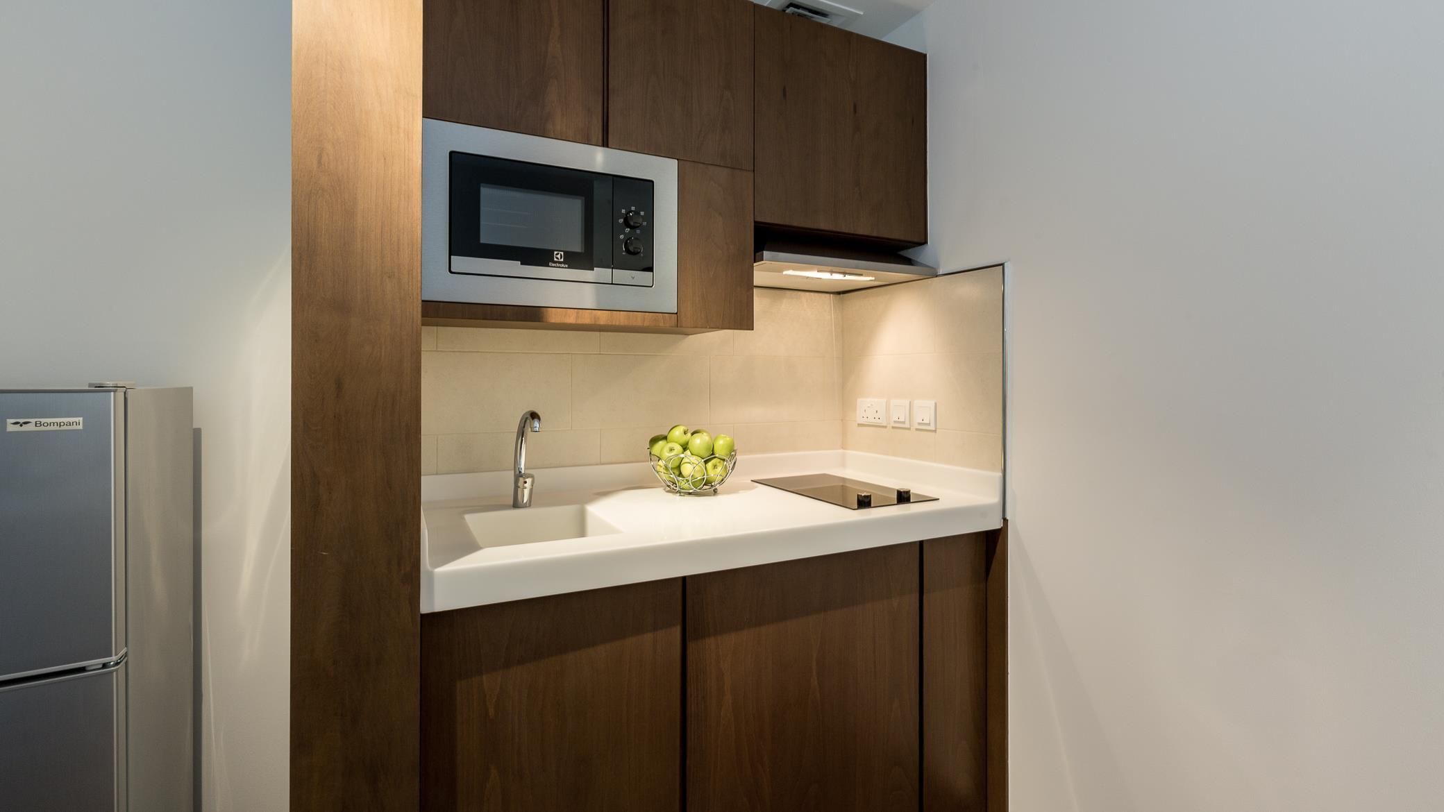 A modern kitchen with a built-in microwave, a stainless steel refrigerator, and a white countertop.
