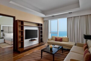 Una sala moderna con televisor de pantalla plana montado en un mueble de madera, un sofá, una mesa de centro y un amplio ventanal con vista al mar.