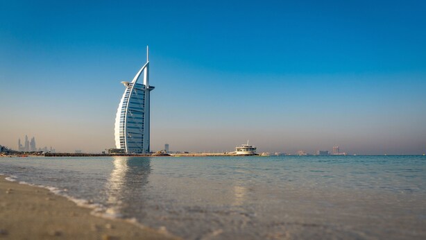 A modern, curved hotel by the sea with a clear view of the water and distant city skyline. - La Suite Dubai Hotel & Apartments Operated by Minor Hotels (Dubai)