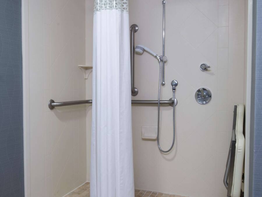 A walk-in shower with a white curtain, a handheld showerhead, a handheld shower head, and a wall-mounted faucet.
