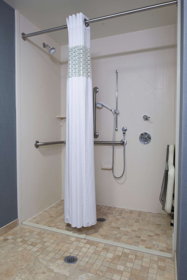 A walk-in shower with a white curtain, a handheld showerhead, a handheld shower head, and a wall-mounted faucet.