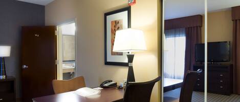 A hotel room with a desk, chairs, a lamp, a telephone, and a television.
