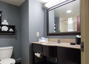 A bathroom with a toilet, a sink with a mirror, and a towel rack with towels. - Hampton Inn & Suites Vineland (Vineland)