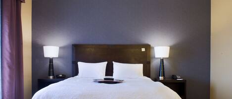 A hotel room with a large bed, two bedside tables with lamps, and a dark headboard.