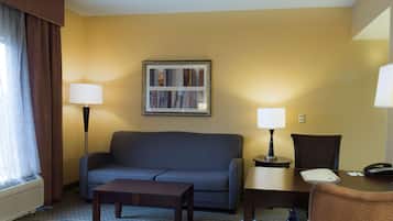 A hotel room with a sofa, a small table, a lamp, a chair, and a framed picture on the wall.