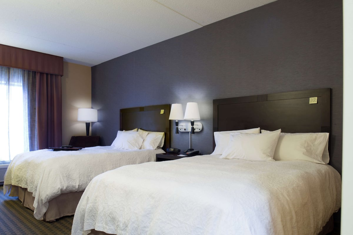 A hotel room with two beds, each with white linens, a nightstand with a lamp, and a headboard with a control panel.