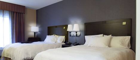 Habitación de hotel con dos camas, cada una con ropa blanca, una mesita de noche con lámpara y cabecero con panel de control.