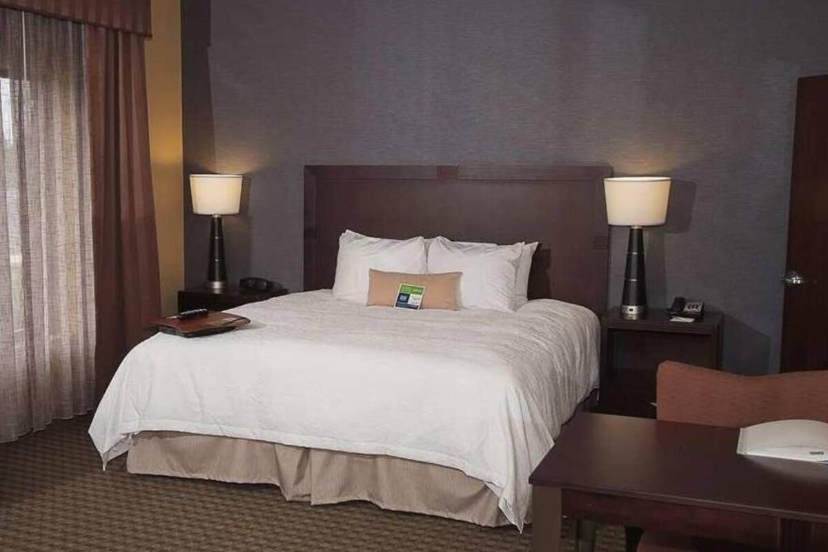 A hotel room with a bed, two bedside tables with lamps, a desk, and a chair.