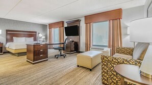 Une chambre d’hôtel équipée d’un lit, d’un bureau, d’une chaise, d’un pouf et d’une télévision.