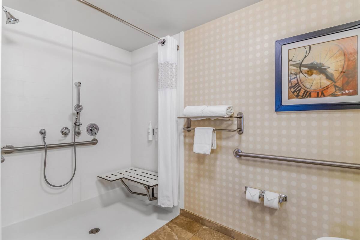 A bathroom with a shower, grab bars, a towel rack, and a toilet paper holder.