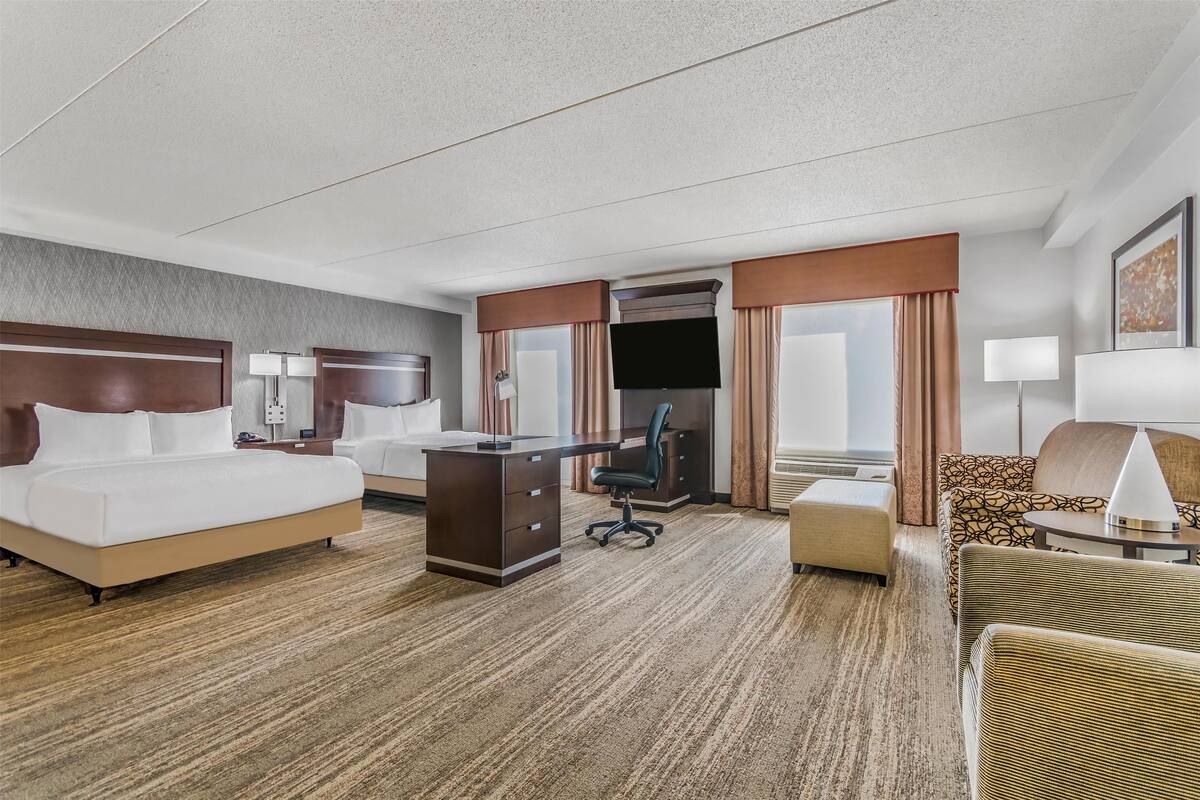 A hotel room with a large bed, a desk, a chair, a sofa, and a TV.