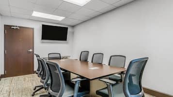 A conference room with a long table, six chairs, a projector screen, and a door.