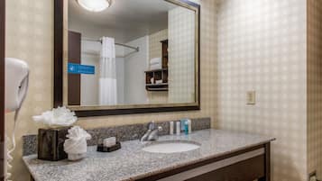 A bathroom with a granite countertop, a sink, a mirror, and a towel dispenser.