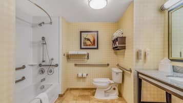 Baño con bañera, inodoro y lavabo. Hay barras de apoyo, un perchero para toallas y un cuadro en la pared.