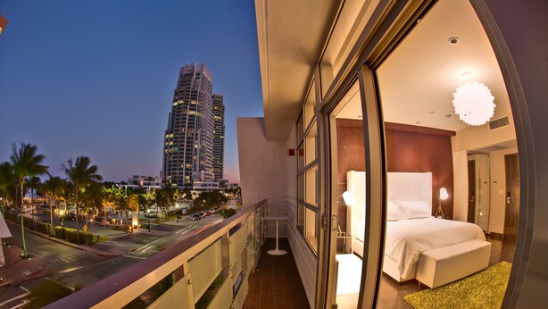 A balcony with a city view, a bedroom with a bed and a nightstand, and a large window.