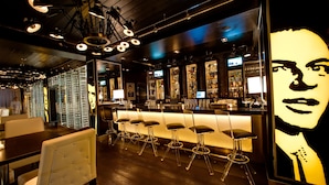 A bar area with a long counter, multiple stools, and a large illuminated portrait on the wall.